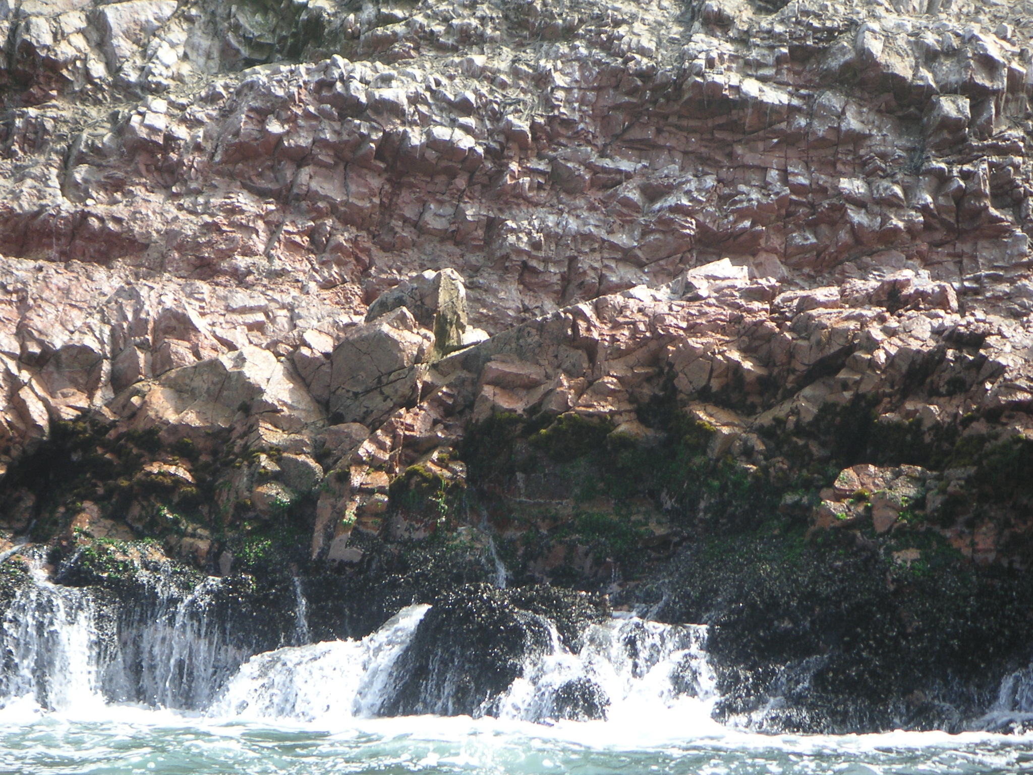 A rocky mountain surrounded by waves.